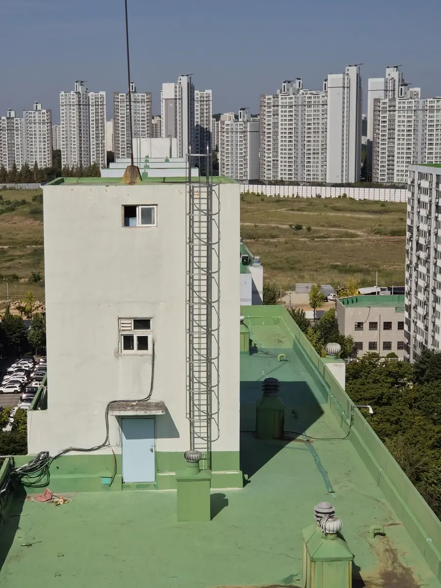 수원 아파트 옥탑방수용 수직안전사다리가 설치된 옥탑 외벽과 도심 전경